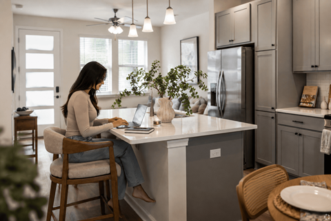 A woman is sitting at a kitchen island using a laptop.