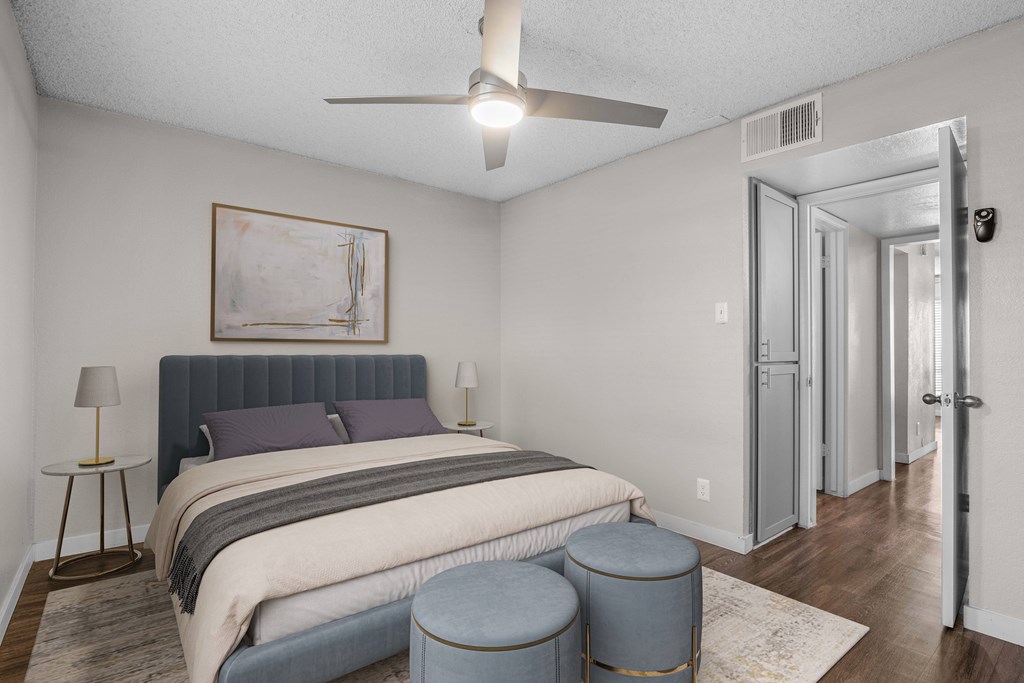 A bedroom with a bed, a painting, a lamp, and a ceiling fan.