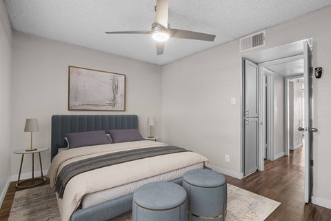 A bedroom with a bed, a painting, a lamp, and a ceiling fan.