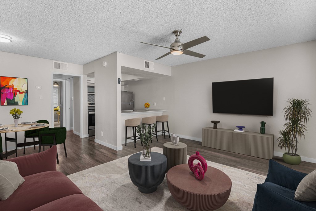 A living room with a red couch, a grey ottoman, and a television on the wall.