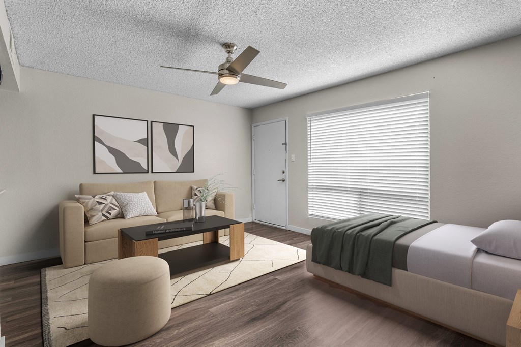 A modern living room with a beige sofa, a coffee table, and a bed with a green blanket.