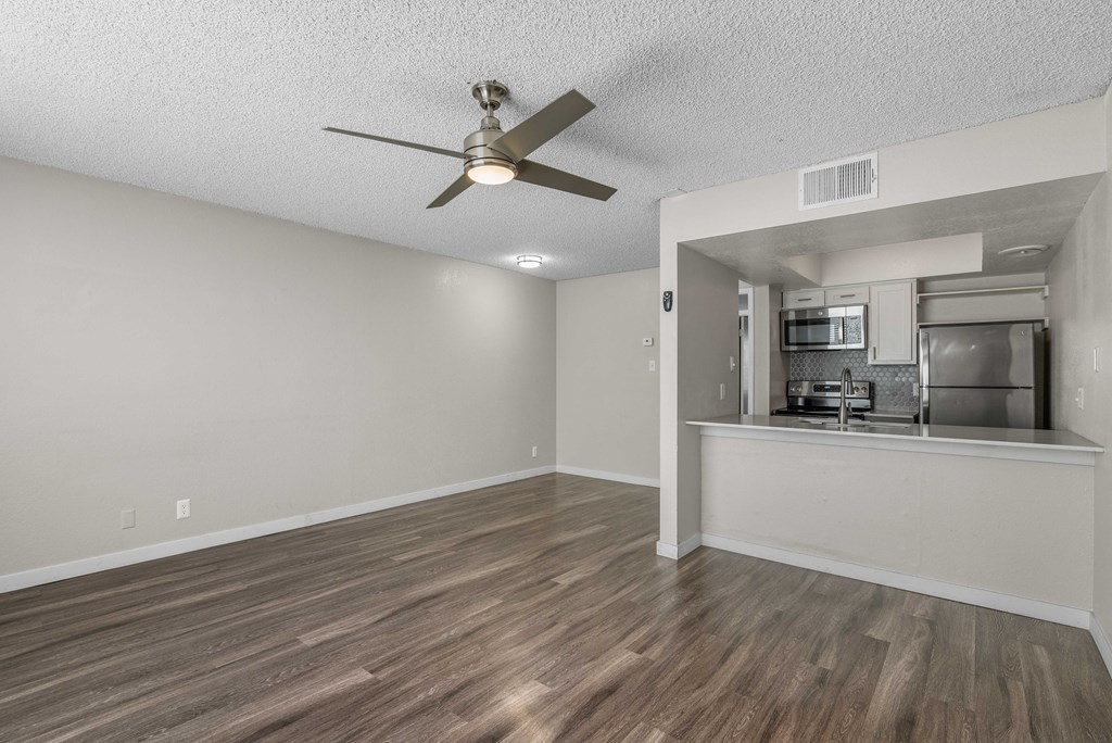 an empty living room with a ceiling fan and a kitchen
