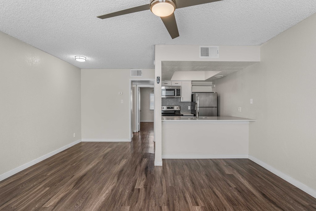 an empty living room and kitchen with a ceiling fan
