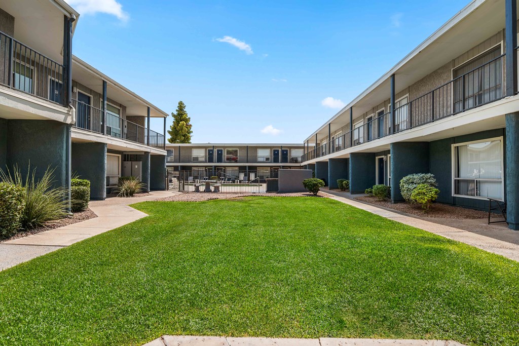 a grassy courtyard between two apartment buildings with a lawn