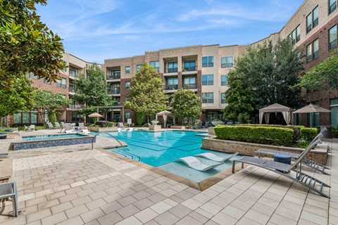 A large swimming pool surrounded by a brick patio and lounge chairs.