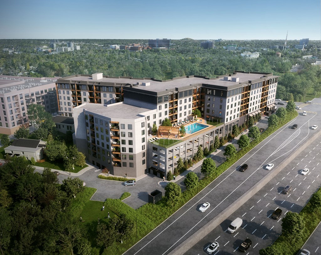 A large, modern apartment complex is situated on a hill with a busy road in front of it.