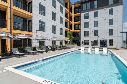 A swimming pool in front of a modern building with lounge chairs and umbrellas.