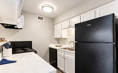A black refrigerator stands in a kitchen with white cabinets and a marble countertop.