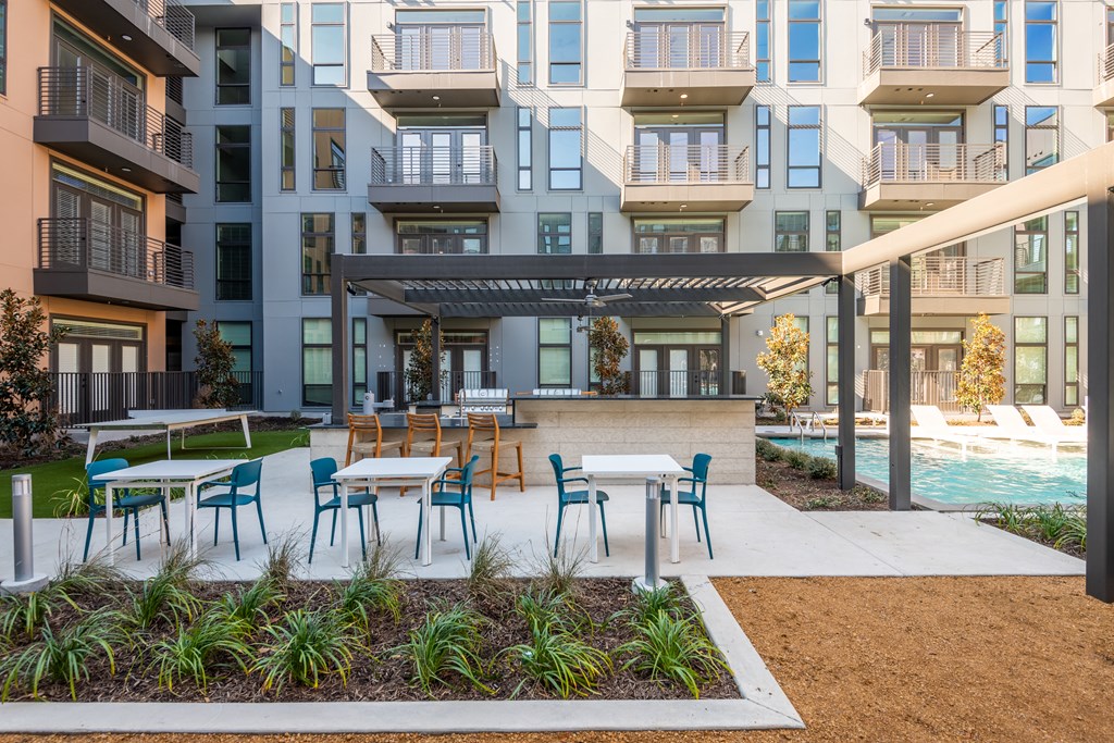 a patio with tables and chairs and a pool in front of an apartment building