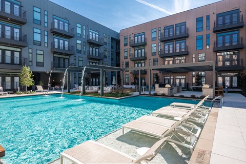 a swimming pool with lounge chairs in front of an apartment building