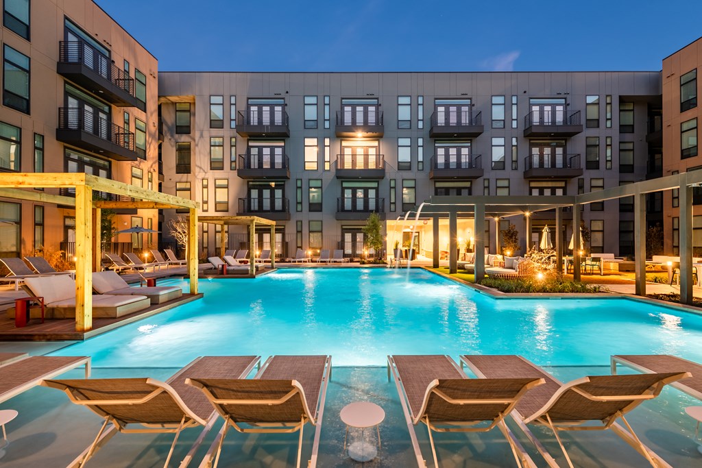 a swimming pool with lounge chairs and umbrellas in front of an apartment building