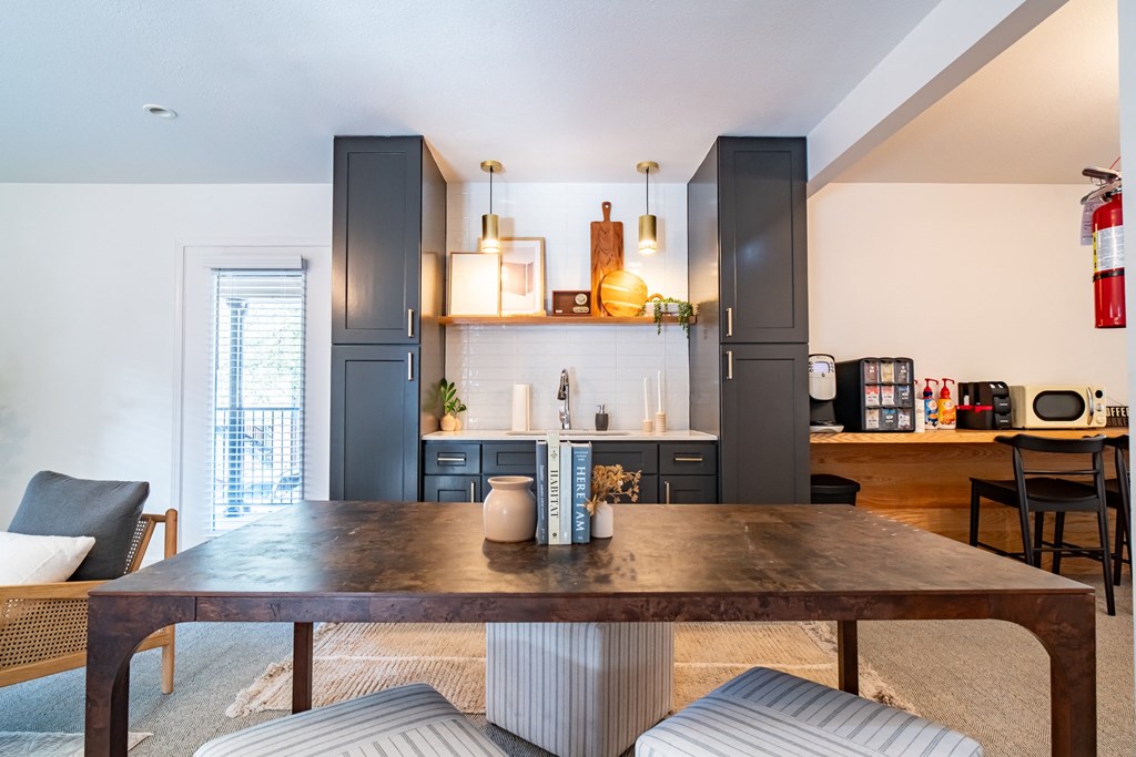 a living room with a wooden table and a kitchen with grey cabinets