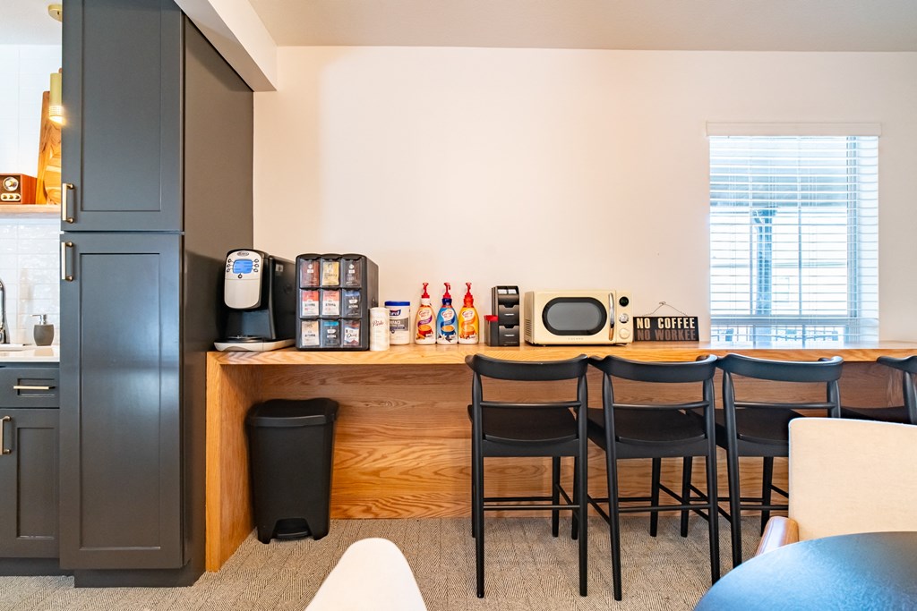 a kitchen with a bar with four chairs and a refrigerator and microwave