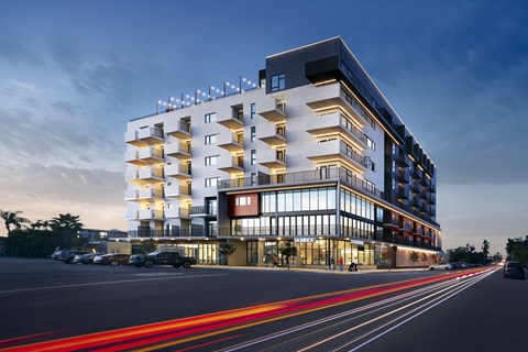 A modern building with a parking lot in front and light trails from moving vehicles.