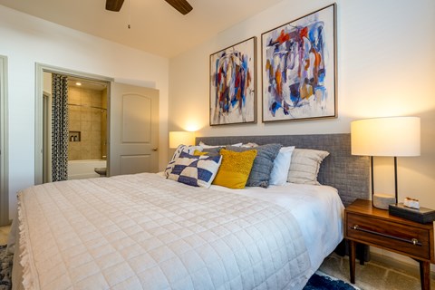A bedroom with a large bed and two abstract paintings on the wall.