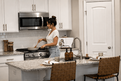 A woman is cooking in a kitchen with a stove and a microwave.
