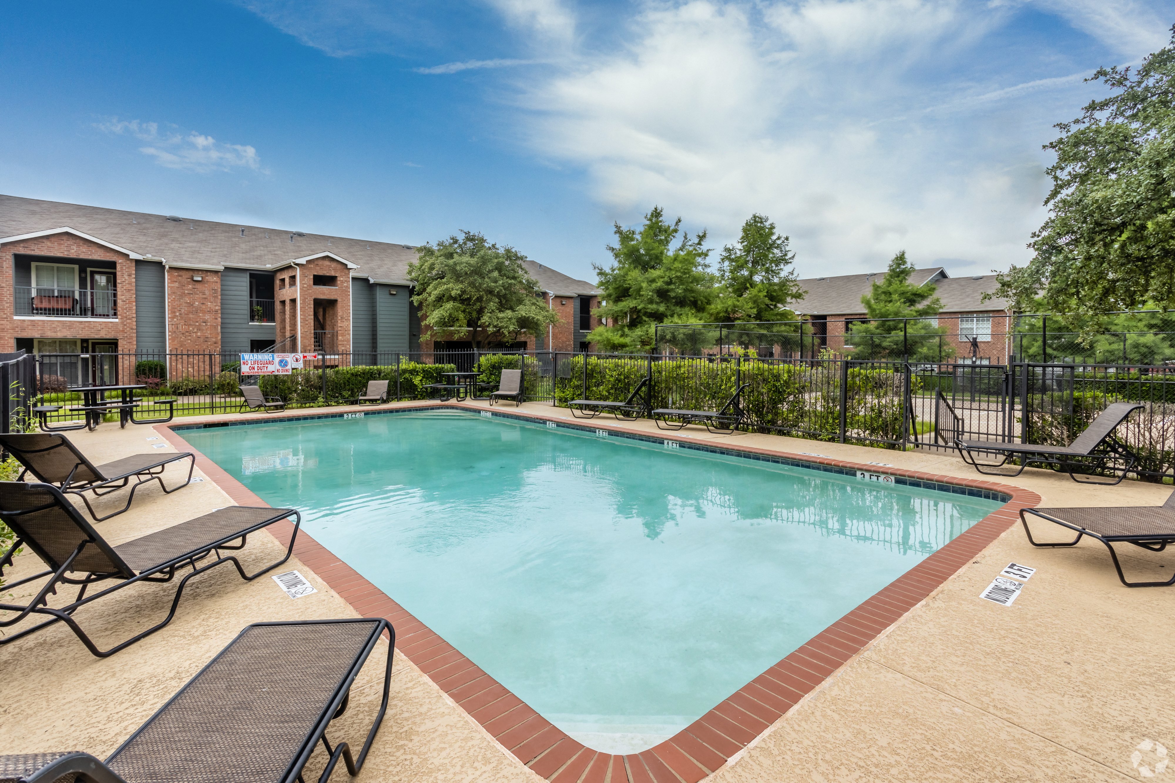 A swimming pool surrounded by lounge chairs and a fence.