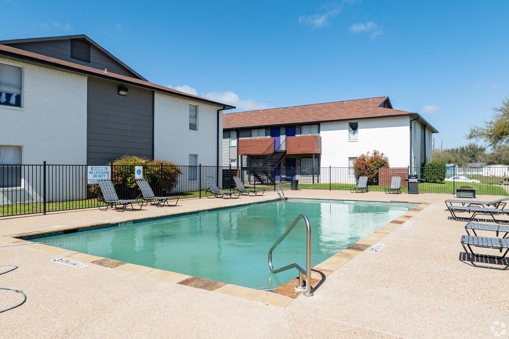 A swimming pool surrounded by lounge chairs and a building in the background.