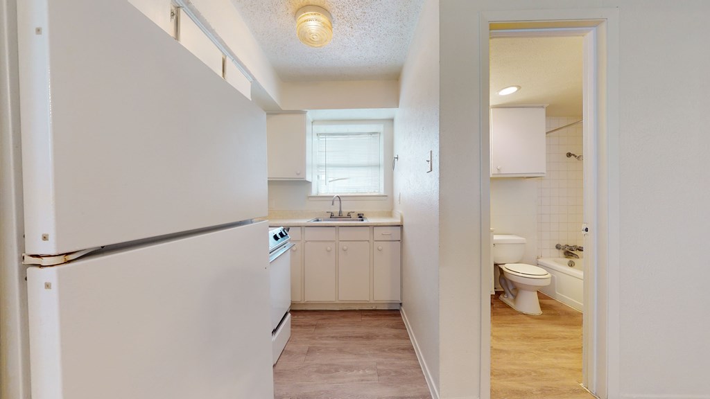 A white kitchen with a refrigerator, sink, and toilet.