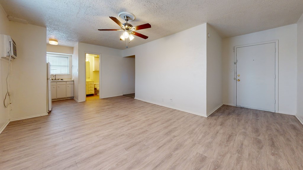 A room with a ceiling fan and light, hardwood floors, and white walls.