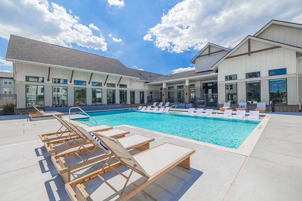 A pool with sun loungers and a building in the background.