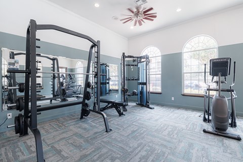 A gym with a variety of equipment including a squat rack, a leg press machine, and a treadmill.