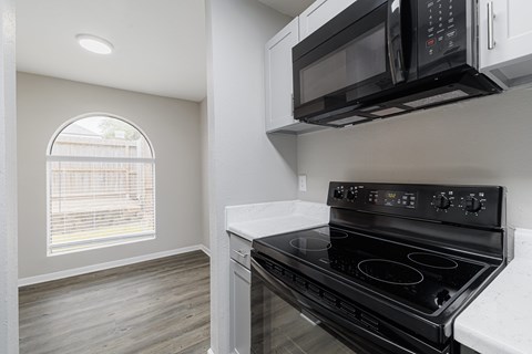 A black microwave oven is mounted above a black stove in a kitchen.
