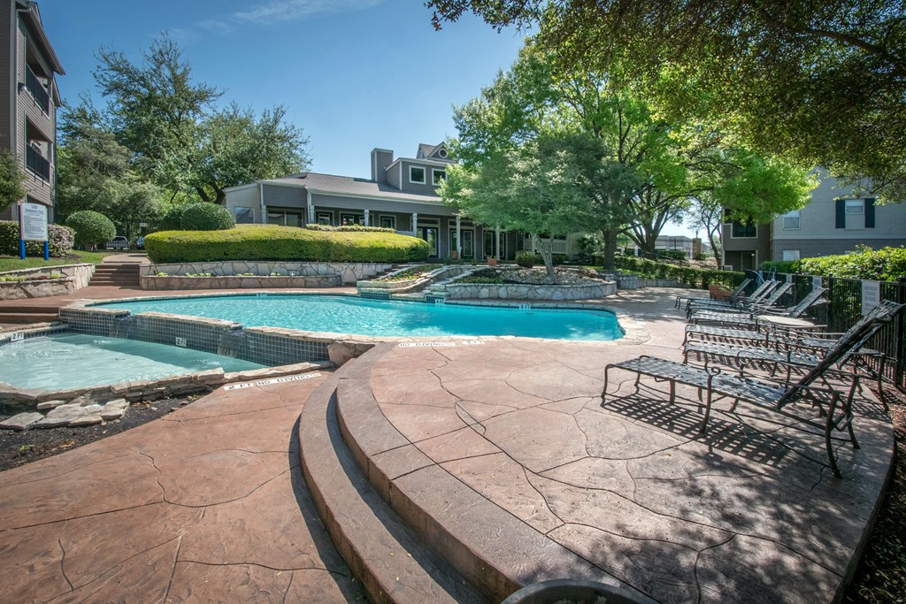 a swimming pool with lounge chairs and a hot tub in front of a building