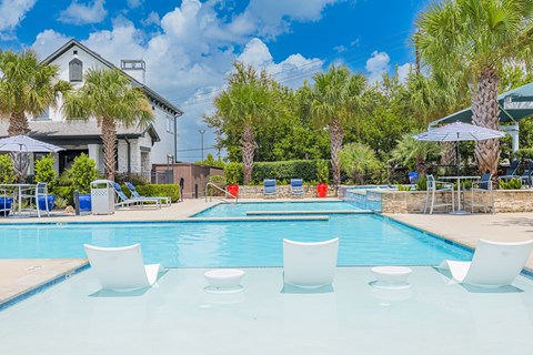 A pool with white chairs and a house in the background.