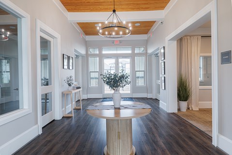 A large, round wooden table is at the center of a spacious room with a chandelier hanging from the ceiling.