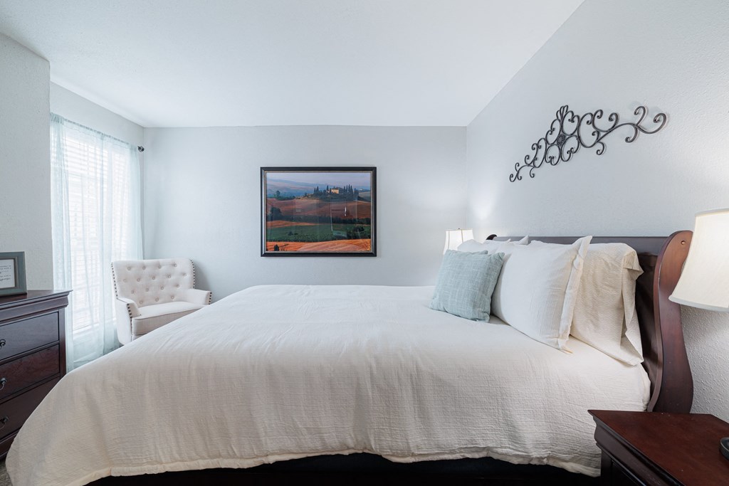 a bedroom with a large white bed and a painting on the wall