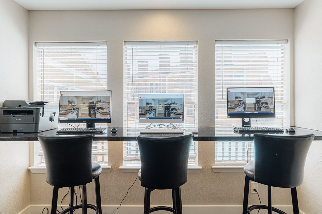 three computers sitting on a desk in front of three windows