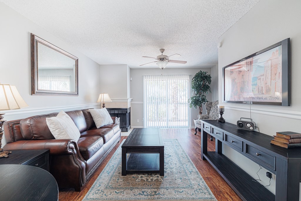 A living room with a brown leather couch, a coffee table, and a ceiling fan.