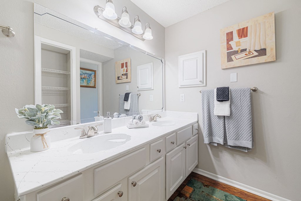 A bathroom with a white counter top and a mirror above it.