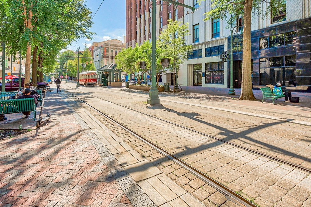 a city street with streetcar tracks and people sitting on benches