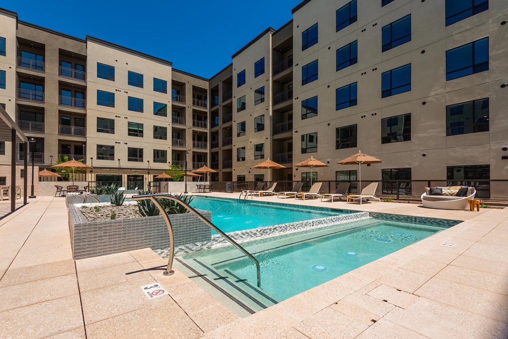 A pool surrounded by apartment buildings and lounge chairs.