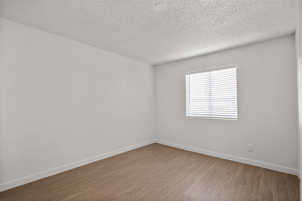 the spacious living room of an apartment with wood flooring and a window
