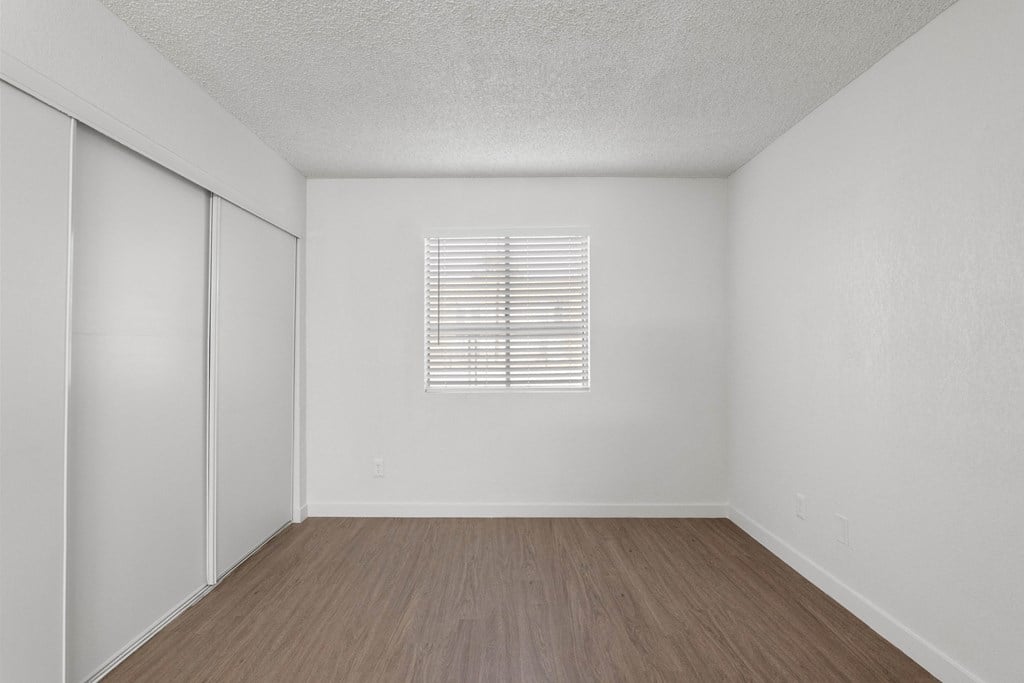 the spacious living room of an apartment with white walls and wood flooring