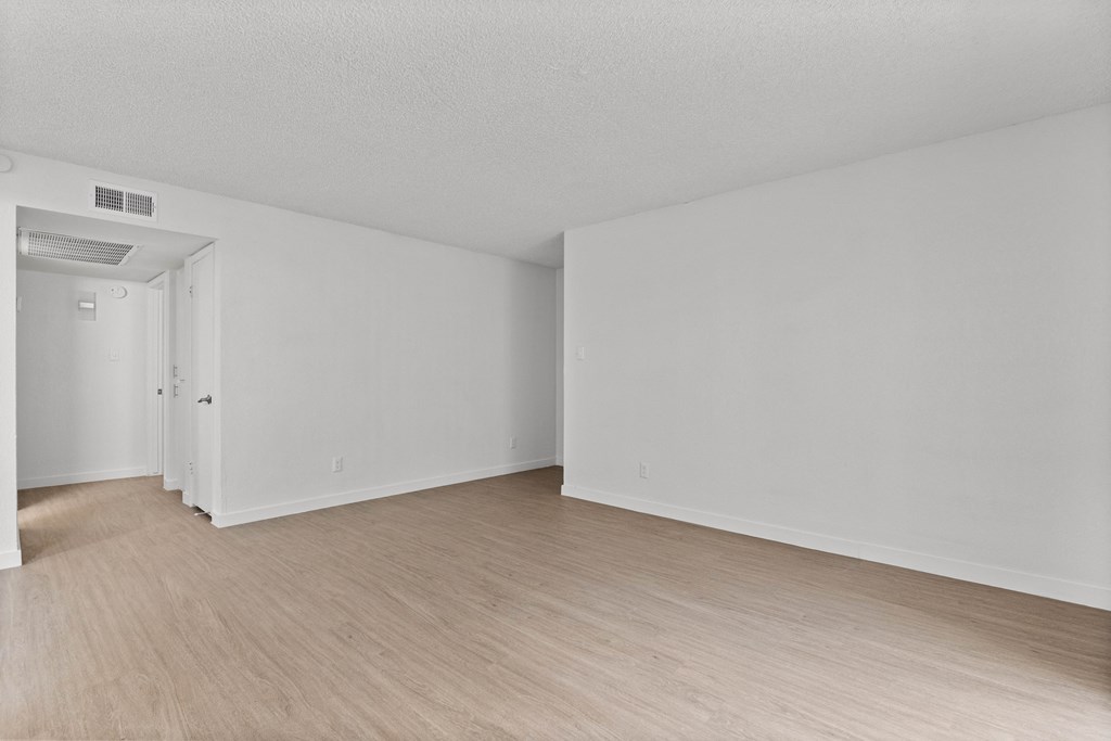 a spacious living room with white walls and wood flooring