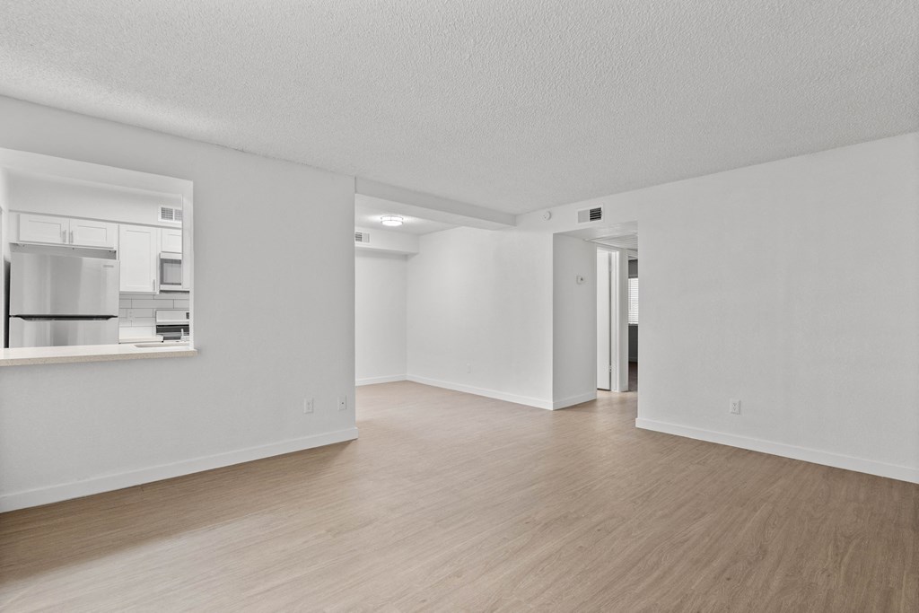 the living room and kitchen of an apartment with white walls and wood flooring