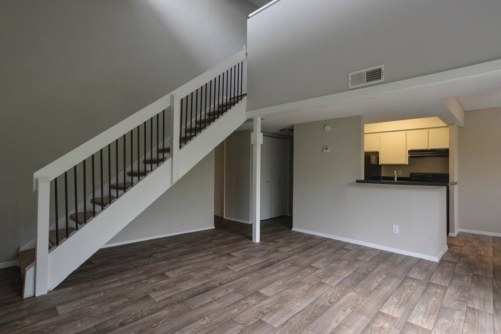 an empty living room with stairs and a kitchen