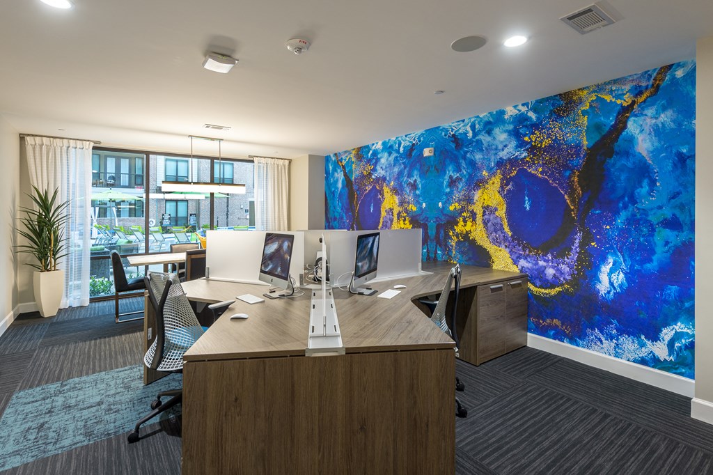 an office with a large desk with two computers and a wall with a blue mural