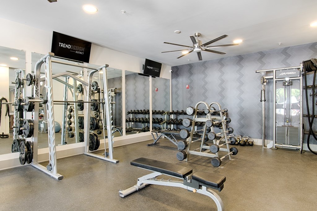 A gym with a variety of equipment including dumbbells, weight plates, and a bench press.