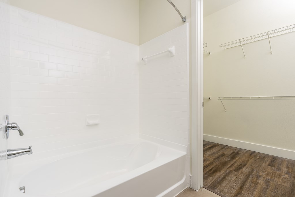 A white bathroom with a tub and a wooden floor.