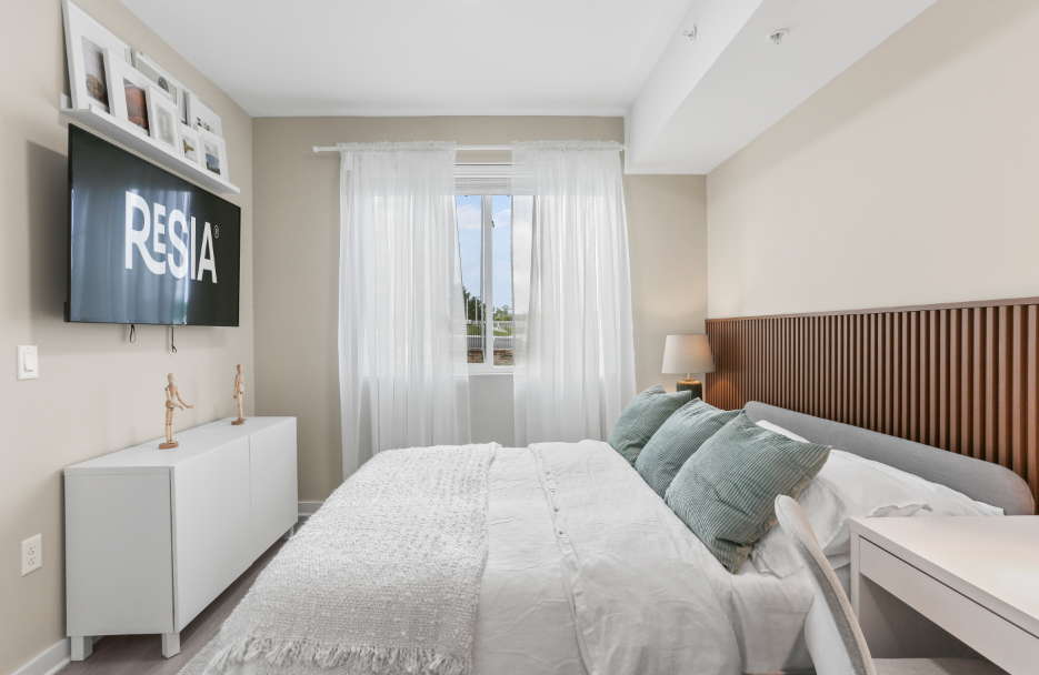 A bedroom with a large bed, a television, and a window with curtains.