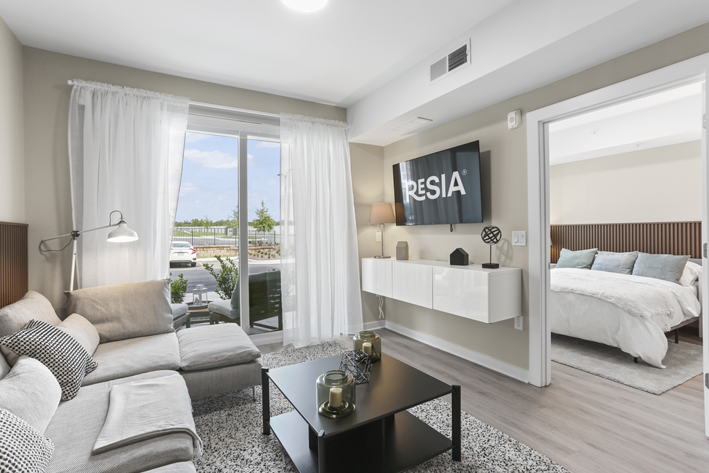 A living room with a large window, a sofa, a coffee table, and a bed.