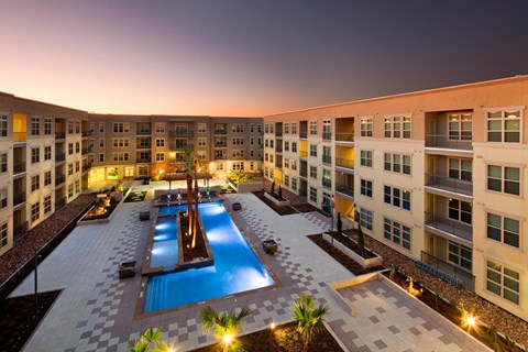 A large swimming pool is surrounded by a tiled patio and palm trees.