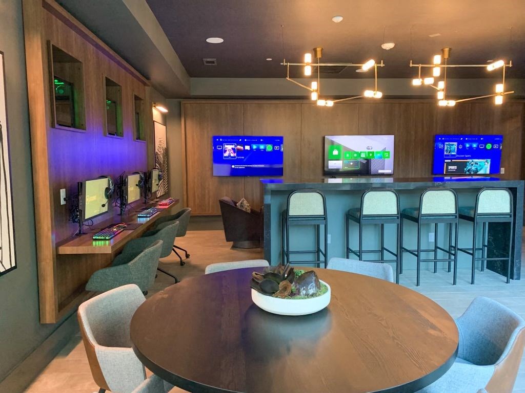 a room with a table and chairs and several televisions on the wall