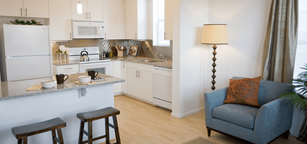a living room with a couch and a kitchen with a sink and refrigerator