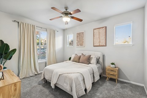 A bedroom with a large bed, a ceiling fan, and a window with curtains.